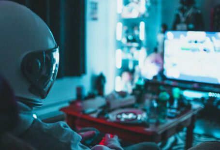 Reality TV Shows - Side view of unrecognizable person in virtual reality helmet sitting on sofa and playing with gamepad in dark room