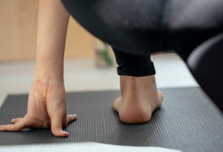 Holistic Approaches - Back view of crop unrecognizable flexible female stretching legs and practicing yoga in Crescent Lunge on the Knee pose at home