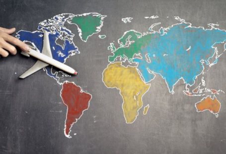 Globalization - Top view of crop anonymous person holding toy airplane on colorful world map drawn on chalkboard
